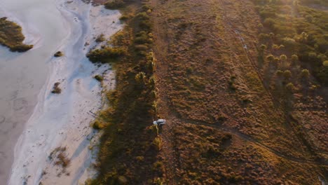 wide dynamic drone shot of white overland vehicle parked on the shore of a lake in progreso yucatan mexico as the sun sets