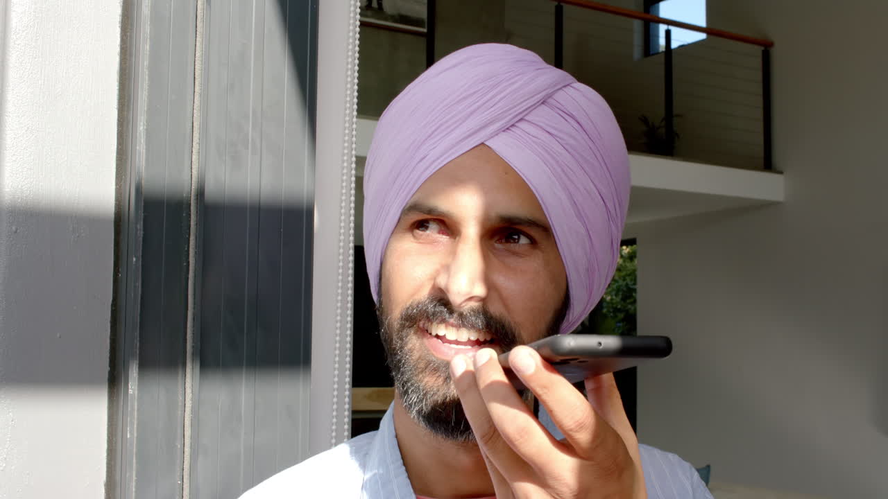 Uomo indiano con turbante che sorride a casa, parlando al telefono.