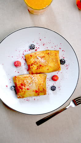 stop motion animation revealing nalysnyky, traditional eastern european crepes garnished with berries and powdered sugar, served on white plate with orange juice