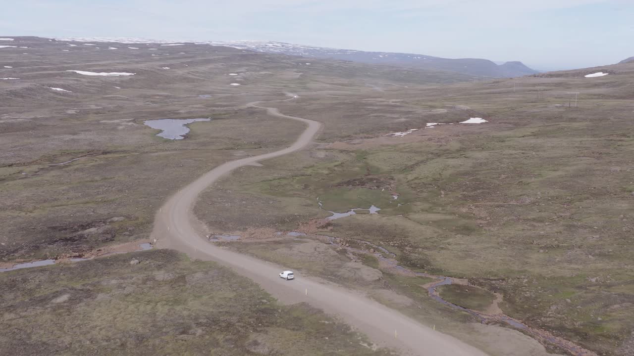 coche blanco conduce por un camino de tierra en un vasto paisaje escarpado del este de islandia, aéreo