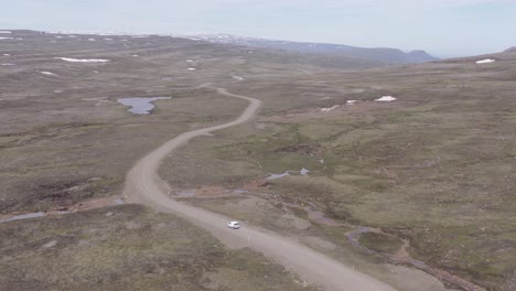 White-car-drives-on-dirt-road-in-vast-rugged-landscape-of-East-Iceland,-aerial