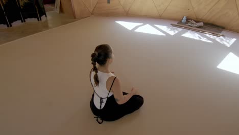 calming yoga session in a zen geometric studio with a latina woman, practicing mindful stretching poses seated in middle of studio, view from behind