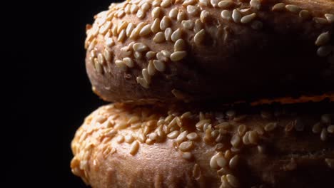 fresh bagels with sesame seeds in rotation. black background. extreme closeup.