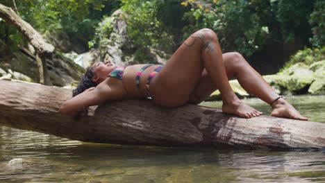 a bikini girl laying on a fallen log in a river on a sunny day in the caribbean