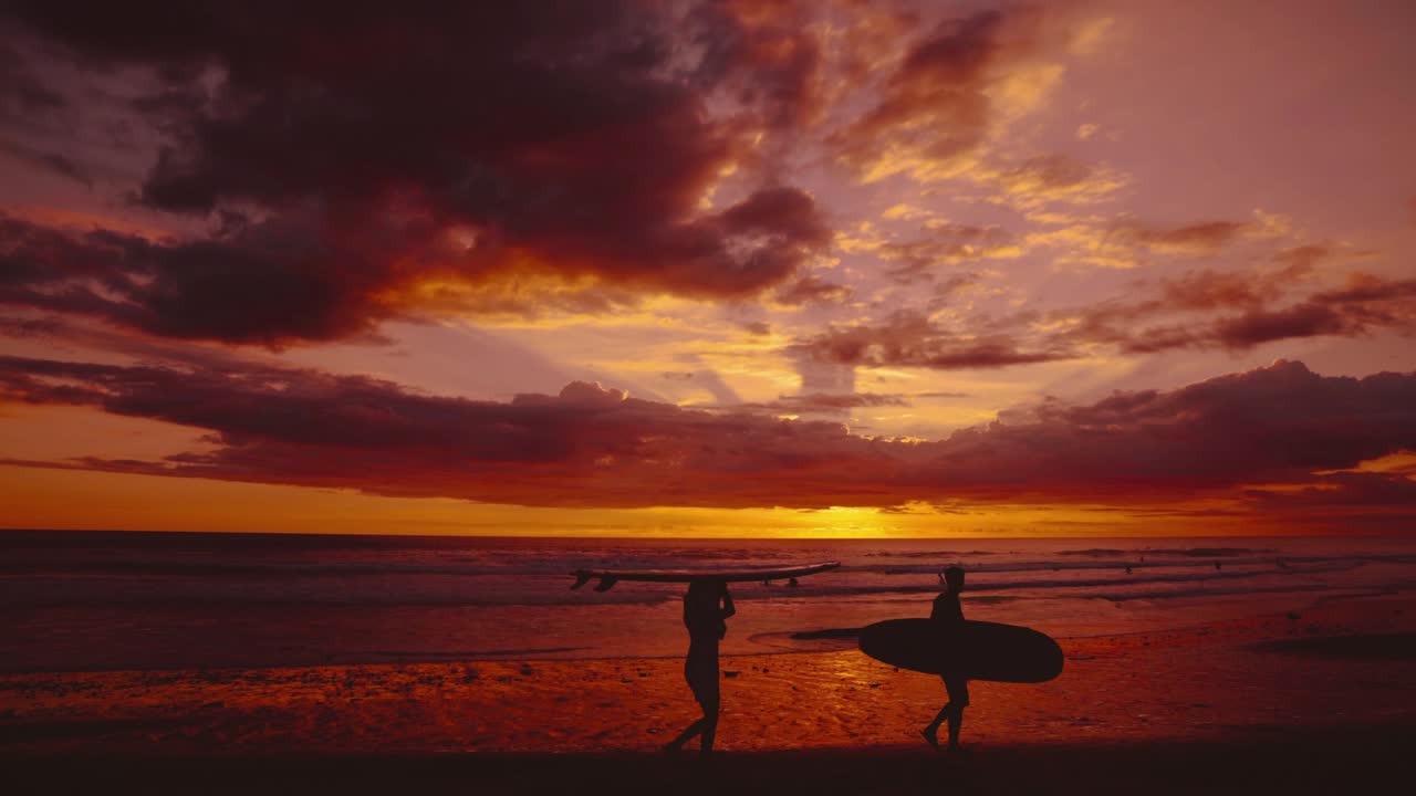 Cinemagraph / seamless video loop of surfers with surfing boards at a remote natural Sri Lanka seaside sand beach with vibrant red sunset dramatic sky and panoramic sea view. Blue and turquoise water at the scenic nature tourist vacation