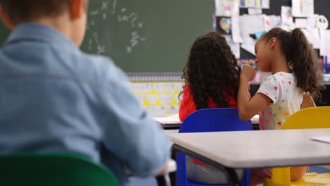 vista trasera de escolares de raza mixta susurrando en el oído de sus compañeros de clase en el aula 4k
