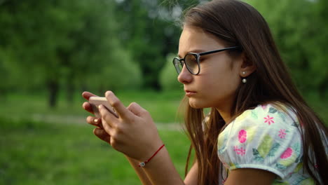 Cierra-A-Una-Chica-Seria-Enviando-Mensajes-De-Texto-En-Un-Teléfono-Inteligente-En-El-Parque-De-Verano.