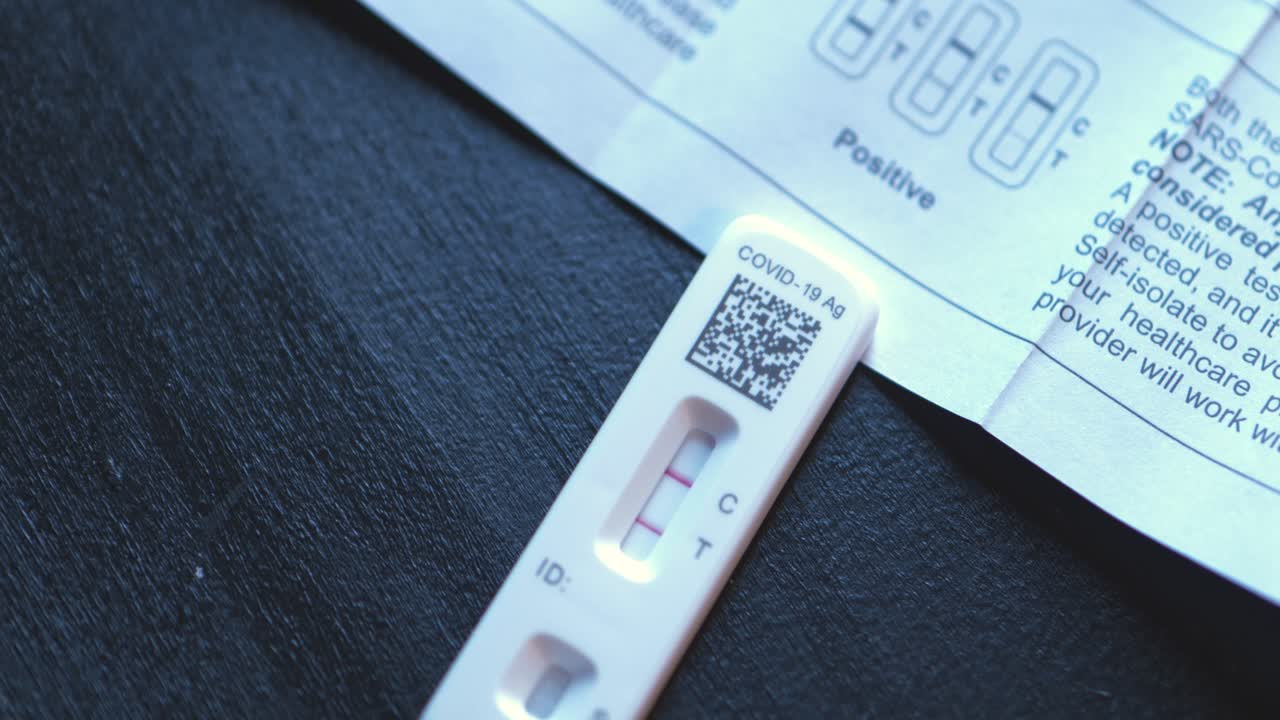 Covid 19 positive at home test kit on black table with instruction book pamphlet showing how to find positive results with two red lines close shot panning around and up with transition out.
