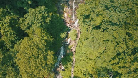 Imágenes-épicas-De-Drones-De-Personas-Caminando-Sobre-Un-Puente-Peatonal-En-La-Base-De-Las-Cataratas-Amicalola,-Una-Cascada-De-729-Pies