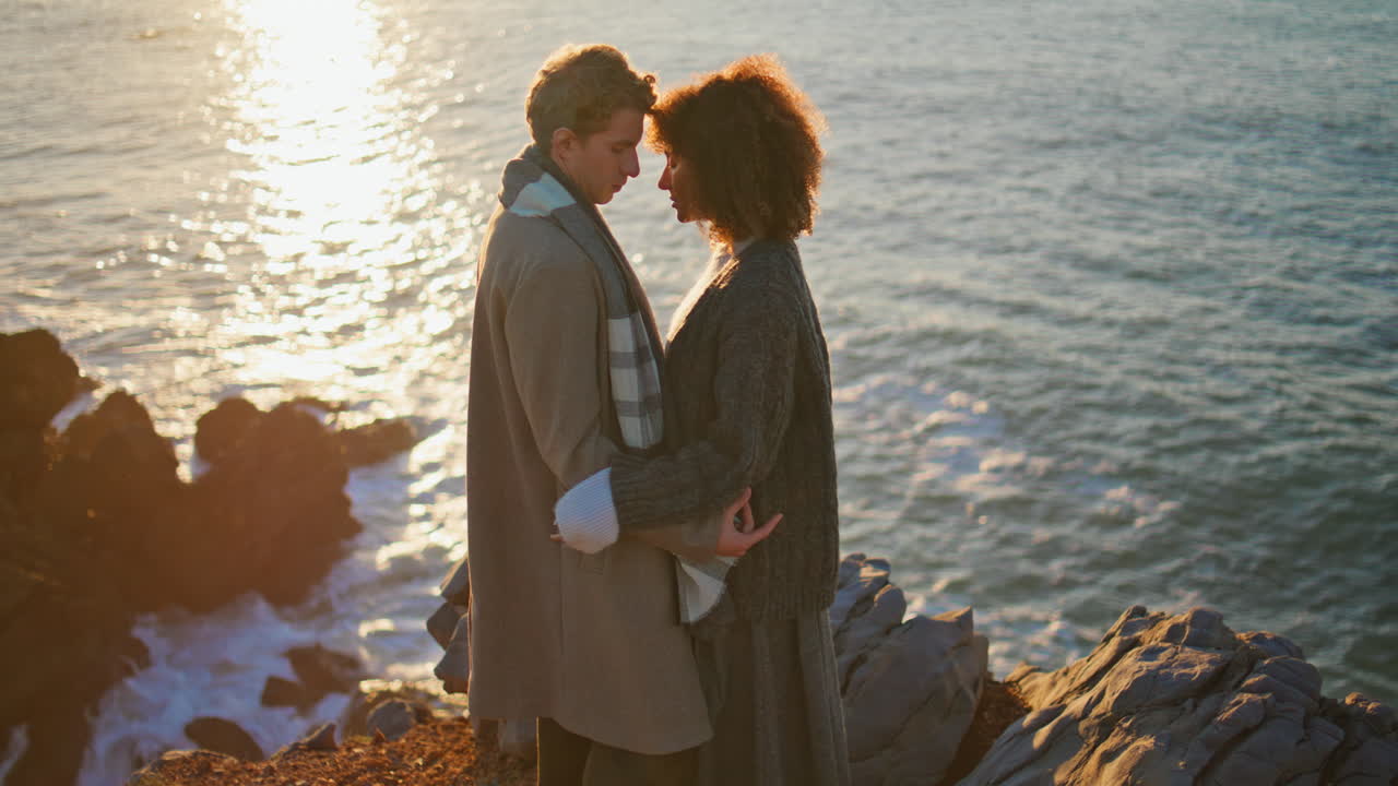 Diverse spouses bonding evening standing on sunny seacoast. Lovers embracing