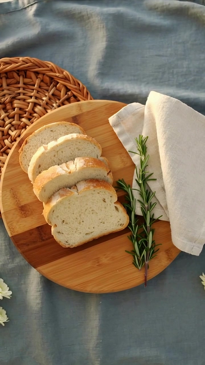 Vertical video: Shifting camera down right as frames play on blue cloth, centering loaf with herb