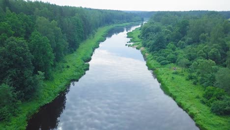 aerial view of a venta river on a sunny summer day, lush green trees and meadows, beautiful rural landscape, wide angle drone shot moving forward