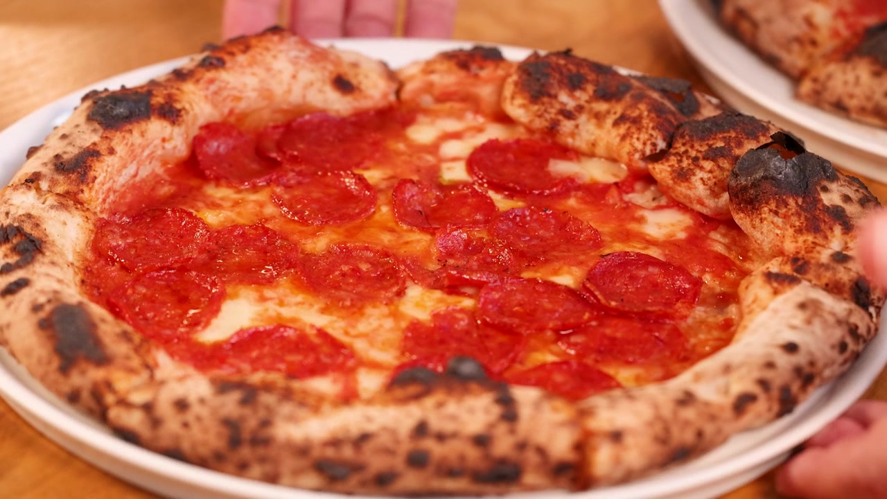 Primo piano di mani che posano una pizza calda al salame piccante con crosta bruciacchiata su un tavolo