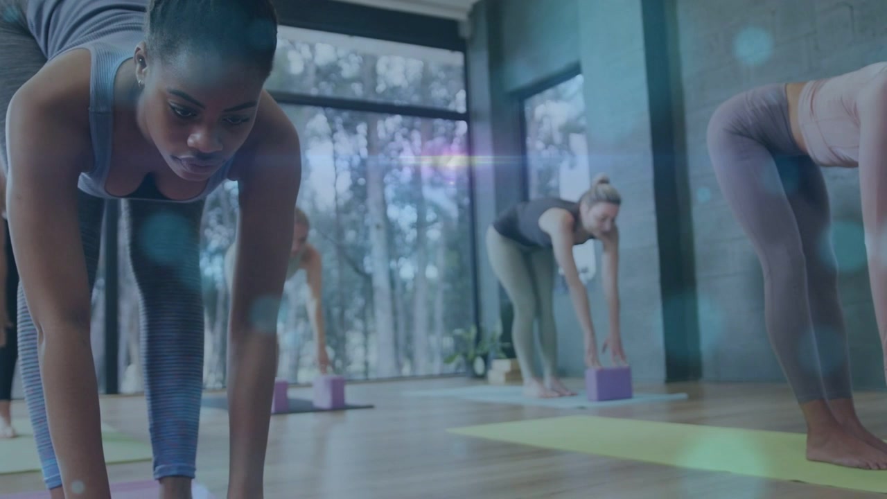 Lead deepening fold after cue, aligning yoga form, peers using purple blocks, blue bokeh overlaying
