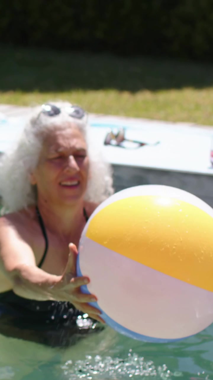 Vertical video: Pal lifting ball to woman in black swimsuit catching in play at dock, purple float