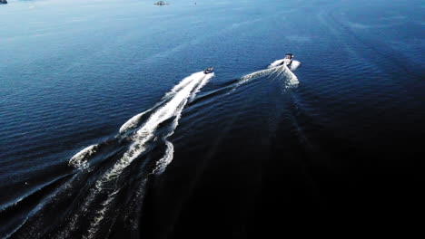 4k aerial shot of motor boats speeding along a blue lake on a sunny day