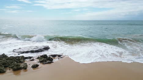 waves crashing on a sandy beach with rocky formations in algarve, portugal