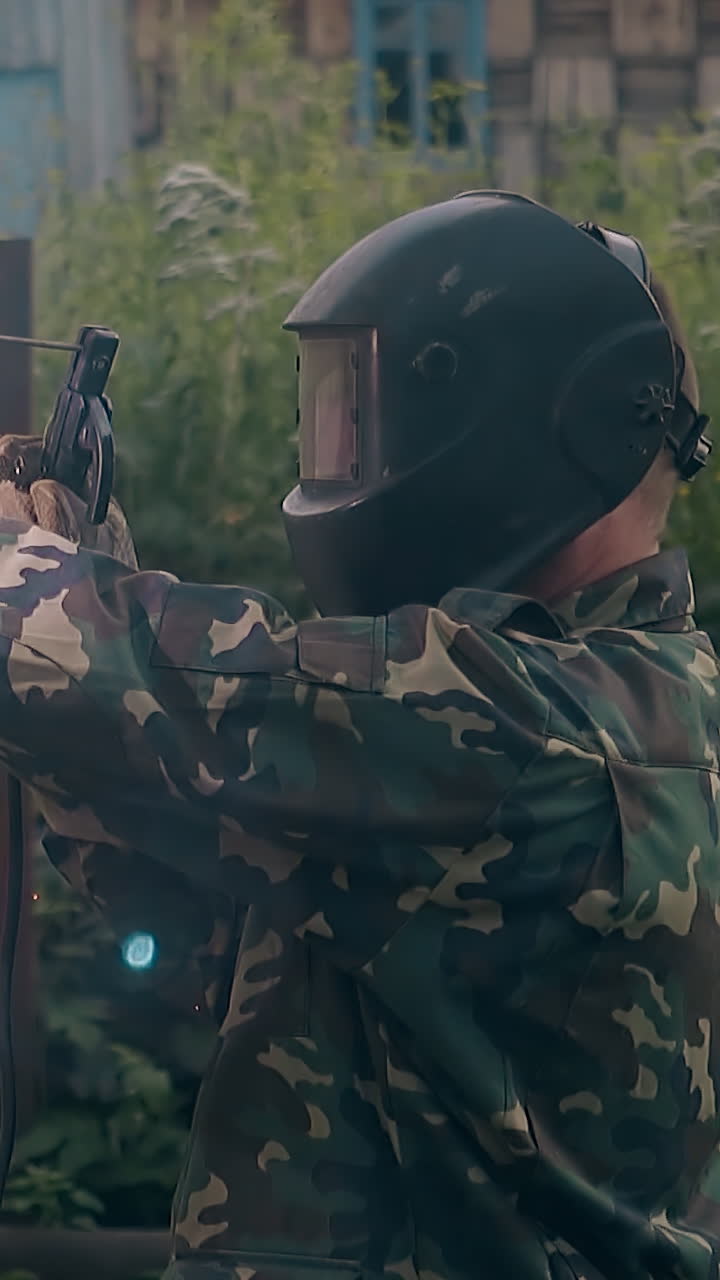 slow motion side view worker in protective mask and gloves welds metal carcass of fence at county house