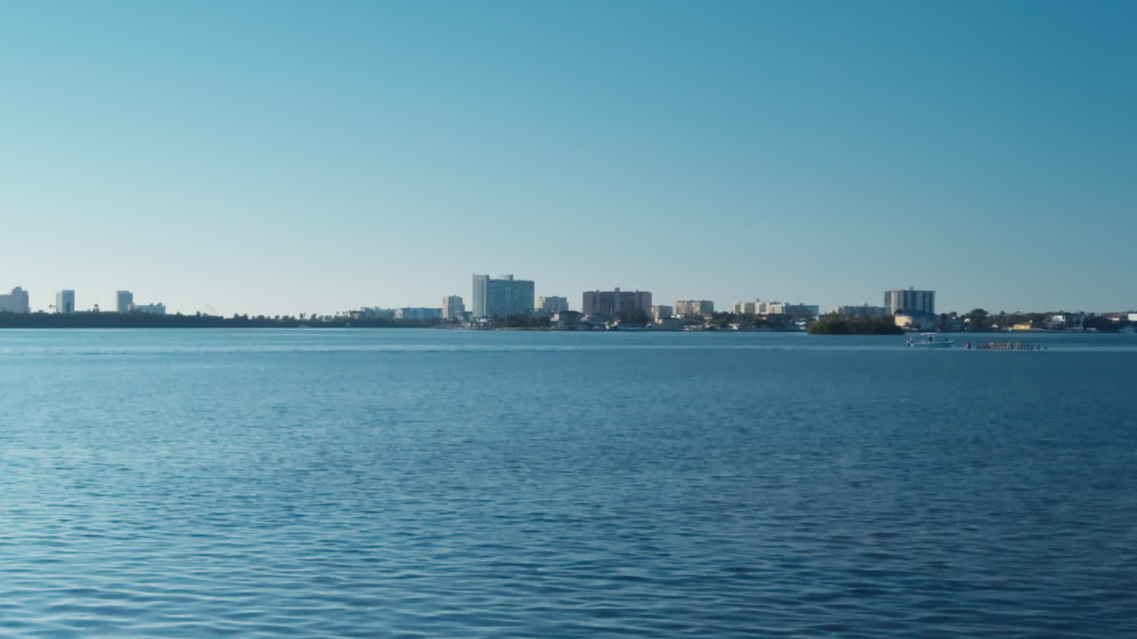 Clearwater Florida skyline sits above shimmering bay water with calm surface textures under bright sunlight, establishing static, empty water