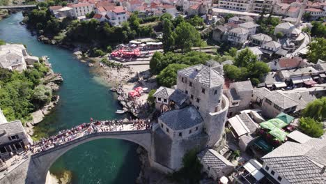 Aerial-view-circling-Stari-Most-bridge,-looking-down-at-people-crossing-Neretva-river-scenic-old-bridge