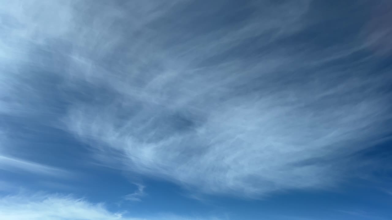 Aerial view from a jet cockpit of some frayed cirrus with a sunny blue sky
