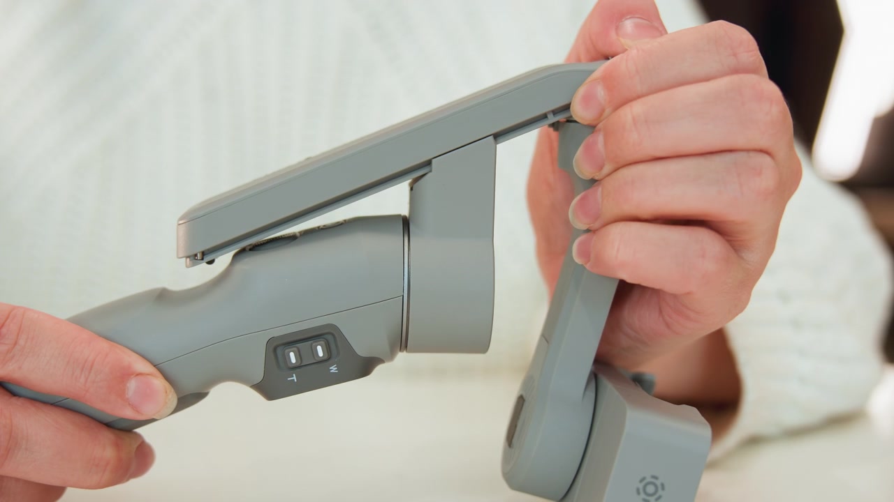 Gros plan horizontal serré de mains insérant une baguette en métal brossé dans le corps mat d'un aspirateur sans fil, avec fermeture du joint, verrouillage du loquet et connexion sécurisée lors de l'installation de l'appareil