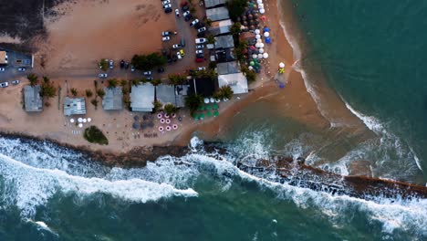 hermosa vista aérea de drones en la parte superior de las olas rompiendo en la costa rocosa tropical con tiendas de playa y sombrillas en la ciudad de tibau do sol cerca de pipa, brasil