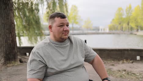 tired young fat man in gray tshirt drinking water from a bottle while sitting outdoors tired young fat man in gray tshirt drinking water from a bottle while sitting outdoors rest during training break pause