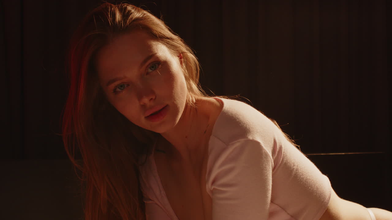 Beautiful portrait of an attractive woman wearing a seductive crop top sensually looking at the camera in a dark bedroom