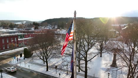 órbita-Aérea-Lenta-Alrededor-De-La-Brillante-Bandera-Estadounidense-Ondeando-En-Un-Día-Soleado-De-Invierno-Con-Nieve-En-Un-Pequeño-Pueblo,-Wellsboro-Pa