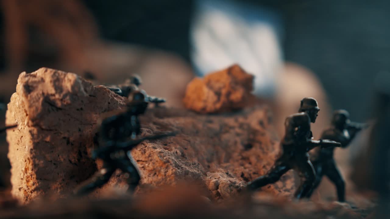 Plastiklegetøjssoldater med geværer løber over en slagmark. Makrobillede af et detaljeret diorama, der genskaber en historisk kampmission.