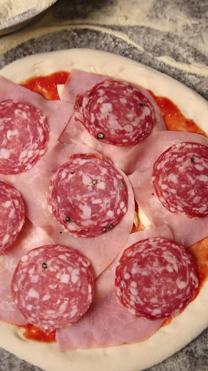 Preparazione di pizza cruda con condimenti di salame, prosciutto e formaggio