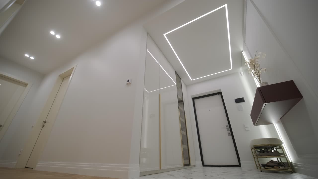 un pasillo moderno iluminado por luces de techo geométricas únicas, con un piso de mármol, que refleja la puerta de vidrio elegante y elementos de decoración elegante, que ofrece una perspectiva de lujo y diseño contemporáneo