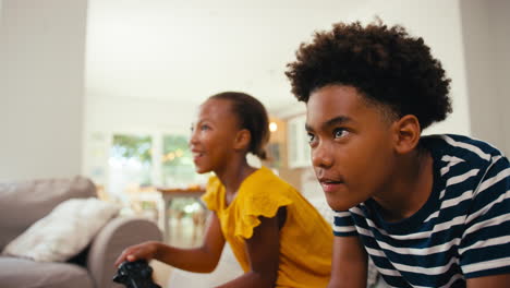 brother and sister sitting on sofa at home playing video game together with girl winning