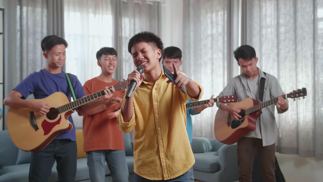 어린 아시아 소년 은 친구 들 이 집 에서 악기 를 연주 하는 동안 스마트폰 에서 노래 를 부르고 가사를 읽는다