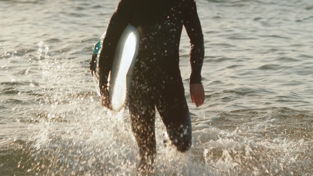 vista frontal de un surfista caucásico adulto corriendo en el mar durante la puesta de sol 4k