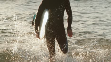 Front-view-of-mid-adult-caucasian-male-surfer-running-in-sea-during-sunset-4k