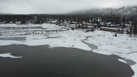 aerial view of people on snow capped coast of big bear lake on cold winter day, california usa, drone shot