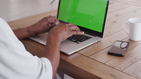 Las-Manos-De-Un-Hombre-Negro-Mayor-Sentado-En-Una-Mesa-De-Madera-Escribiendo-En-Una-Computadora-Portátil,-De-Cerca