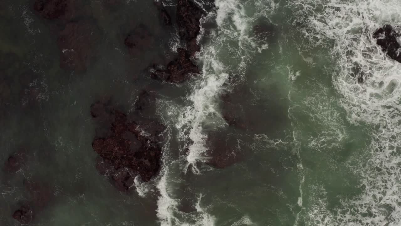 Aerial view Indian Ocean green waves crashing over dark rocky shoreline