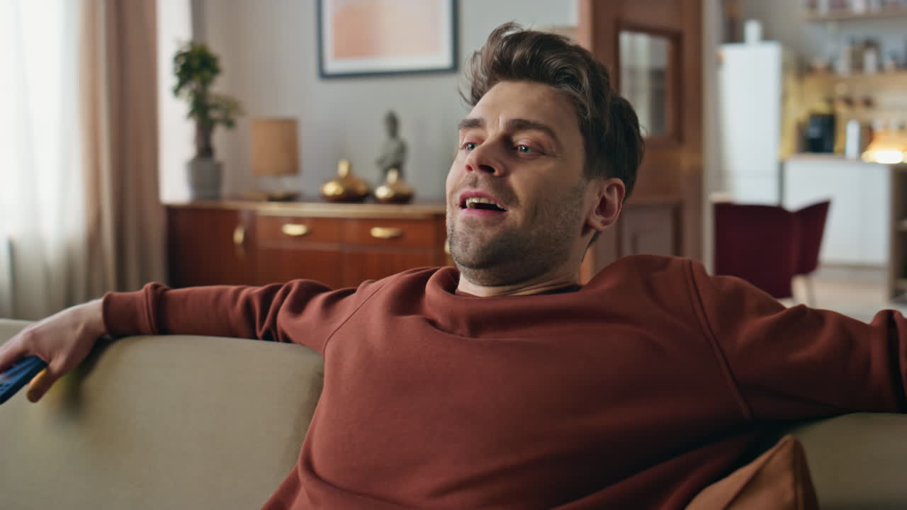 Relaxed hipster falling sofa holding cellphone in modern apartment close up.