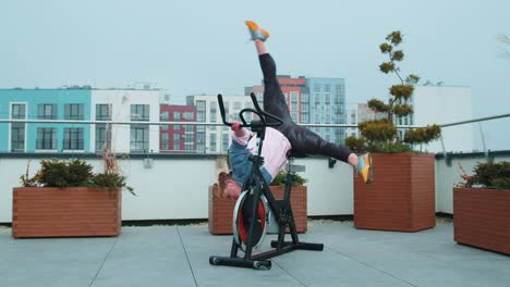 athletic woman makes twine training routine on spin stationary bike on house roof, weight loss