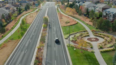 Aerial-view-of-a-single-car-driving-down-a-two-lane-road,-through-a-neighborhood