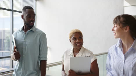 walking in office hallway, diverse colleagues holding laptops and discussing work