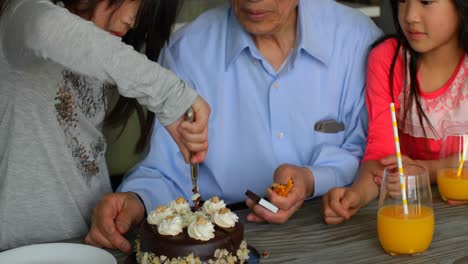 front view of cute asian granddaughter cutting her birthday cake with knife in a comfortable home 4k