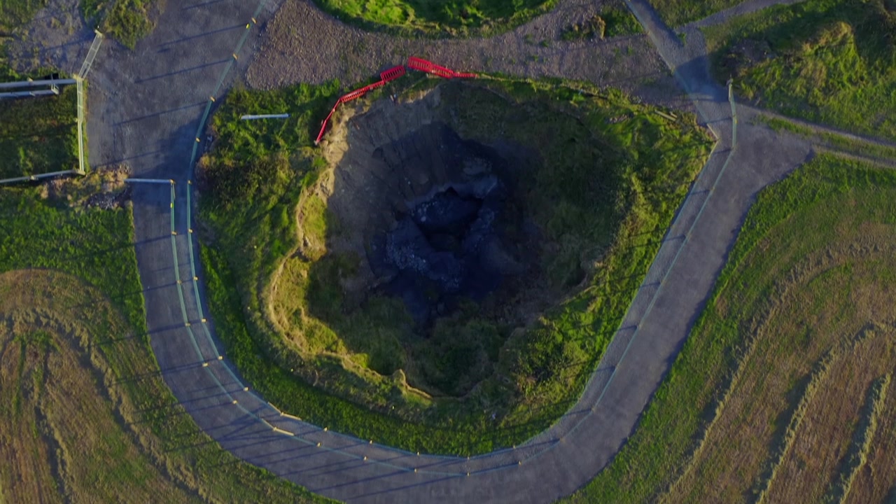 Affascinante ripresa aerea in tilt-down dall'Oceano Atlantico sopra la passeggiata dei Ponti di Ross fino all'iconica dolina, dove la risacca dell'oceano scorre sottoterra.