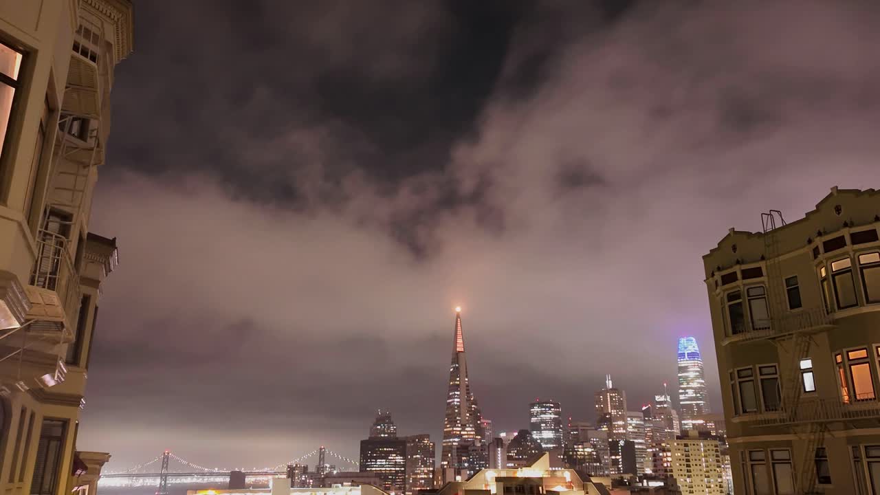A hilltop time-lapse peers down at San Francisco’s skyline and Bay Bridge as city lights flicker into the dusk.