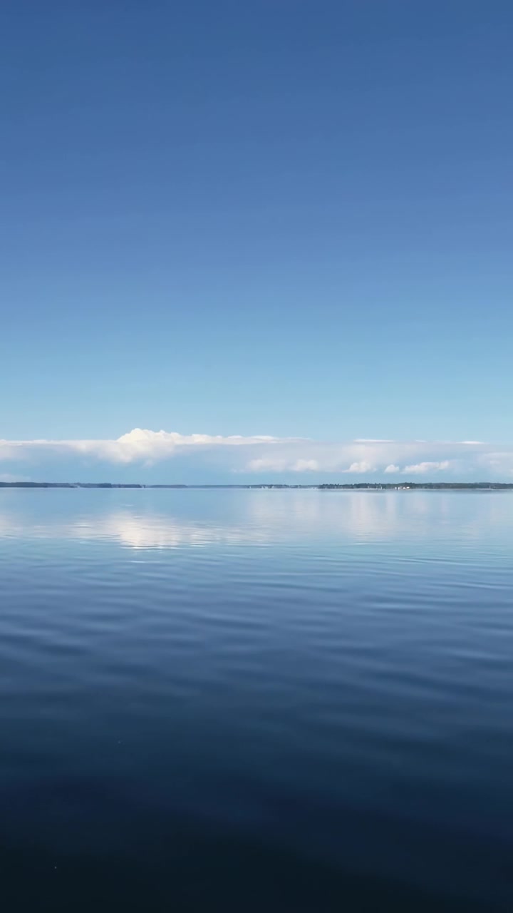 Vidéo verticale: Eau calme et ondulante reflétant une bande de nuages sur une rive basse, changeant sous une légère brise