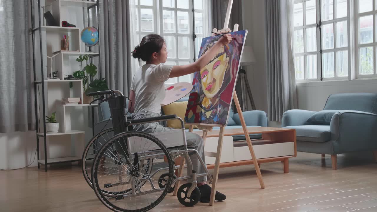 artista femenina talentosa sentada en silla de ruedas, usando con entusiasmo el pincel que crea con pintura al óleo. estudio creativo con lienzo