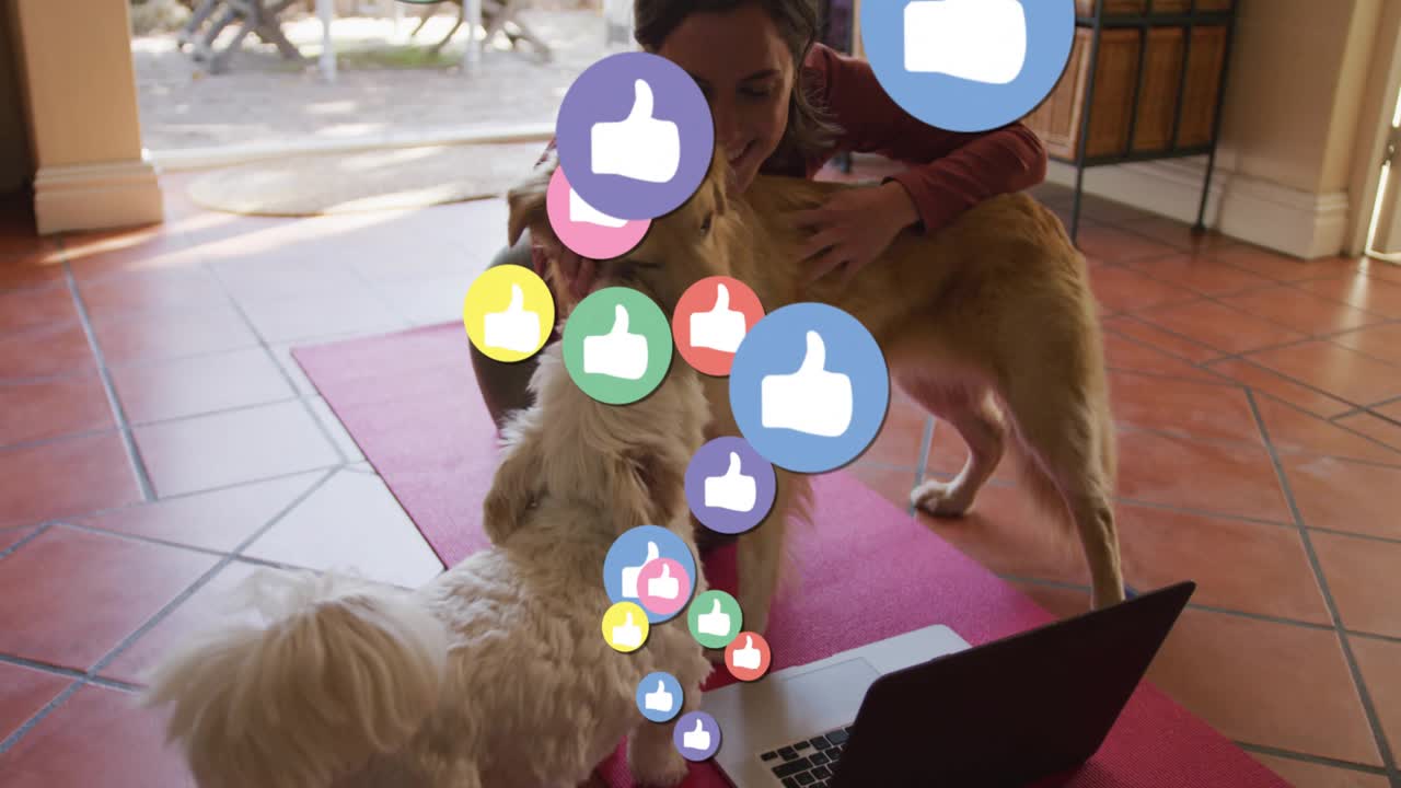 Mujer arrodillada en una esterilla de ejercicios roja acariciando perros junto a un portátil que provoca el aumento de iconos de redes sociales